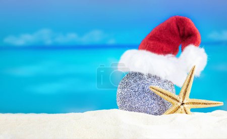 Photo for Shiny silver ball in Santa's hat with starfish on sand of beach. Christmas, New Year. Copy space - Royalty Free Image