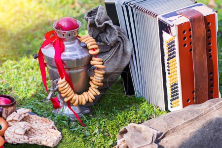 Foto de Composición de picnic o Maslenitsa con bagel, samovar, zapatillas, botón acordeón, bolsa sobre hierba verde. Shrovetide - Imagen libre de derechos