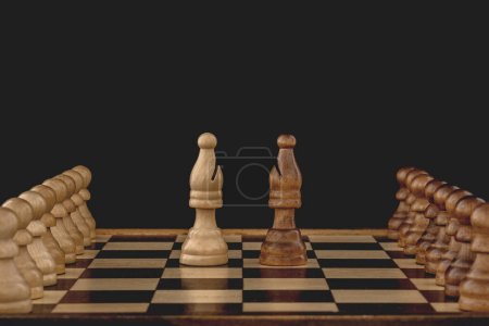 Photo for Concept of rivalry between teams and leaders. Two bishops, each with many pawns following, face off on the chessboard. Black background with copy space. - Royalty Free Image