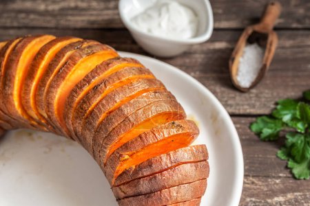 Roasted hasselback sweet potatoes with spices on a wooden table close-up
