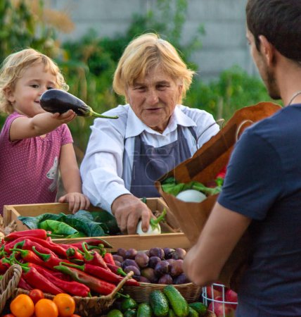 Foto de La abuela y la nieta venden verduras y frutas en el mercado de agricultores. Enfoque selectivo. alimentos. - Imagen libre de derechos