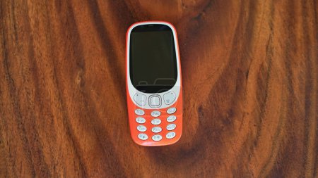Foto de Un teléfono con teclado con botones aislados sobre fondo negro. Teléfono celular viejo con pantalla negra. Primer plano de un móvil naranja de 2g y 3g en la India. Tecnología y concepto social. - Imagen libre de derechos