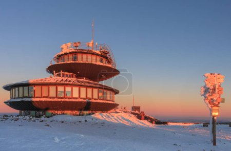 Winter, sunrise time, tourist signposts and disc shaped meteorological observatory in snezka, mountain on the border between Czech Republic and Poland.