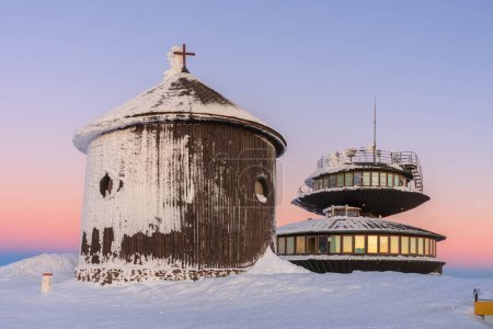 Wooden Roman catholic chapel and disc shaped meteorological observatory in snezka, mountain on the border between Czech Republic and Poland, winter, sunrise time. 