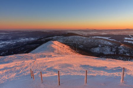 Winter, sunrise time, view from Snezka to pink mountain, krkonose mountain, Czech republic.. Along the road are wooden long bars, tourist markings for winter season. 