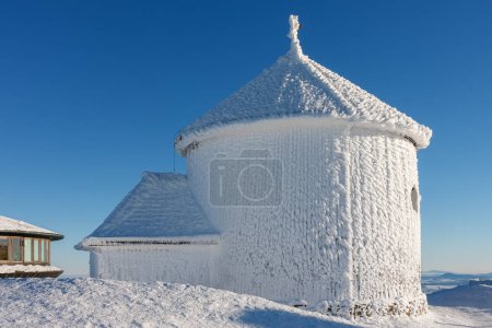 Winter morning , wooden Roman catholic chapel and disc shaped meteorological observatory in snezka, mountain on the border between Czech Republic and Poland. 