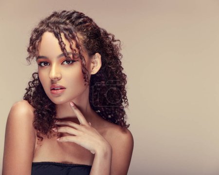Photo for Portrait of a youthful lady with a sweet demeanor, curly locks, set against a beige backdrop - Royalty Free Image
