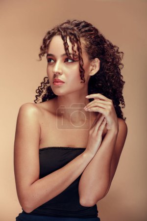 Photo for Woman with curly hair seen in profile, placing her hands together near her chest in a gentle gesture, and with a serene expression on her face - Royalty Free Image