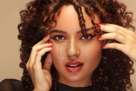 Photo for Intimate close-up of a woman with a gentle countenance, curly locks, adorned with vibrant red makeup, hands delicately framing her face - Royalty Free Image