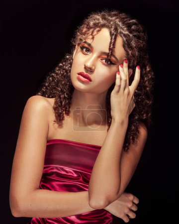 Photo for Woman with curly hair, expressive gaze, hand on face, black background, and red dress - Royalty Free Image