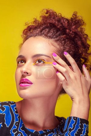 Photo for Close-up of a young woman's profile, with one hand on her face, makeup, against a yellow background. - Royalty Free Image