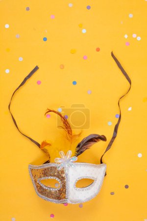 Photo for A golden and white mask adorned with elegant feathers, standing out against a vibrant yellow backdrop - Royalty Free Image