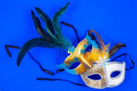 Photo for Two Venetian masks adorned with feathers and sparkling glitter, isolated a captivating blue backdrop - Royalty Free Image