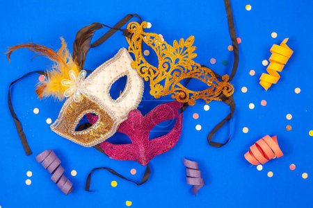 Photo for Three vibrant masks grouped together, standing alone on a blue background adorned with confetti and garlands, creating a lively and festive atmosphere - Royalty Free Image