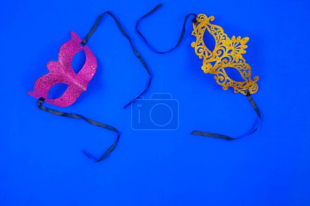 Photo for Two radiant masks, one gilded in gold and the other adorned in violet brilliance, standing alone against a captivating blue backdrop - Royalty Free Image