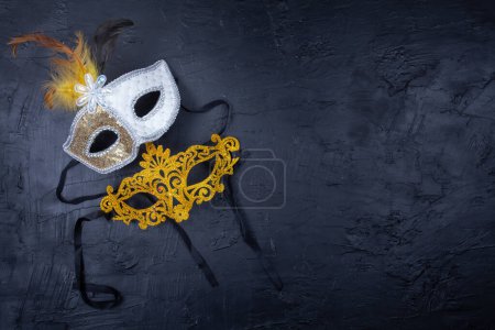 Photo for Two Venetian masks together, one golden and the other white with feathers, placed on a textured black background - Royalty Free Image