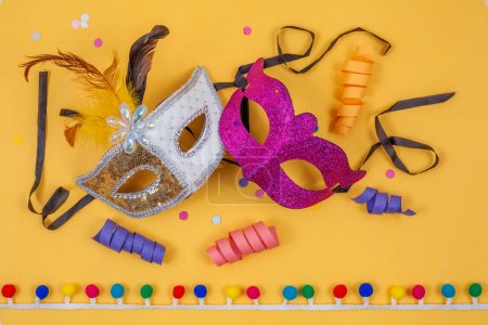 Photo for Venetian carnival masks, colorful and together, isolated on a yellow background adorned with confetti and streamers - Royalty Free Image
