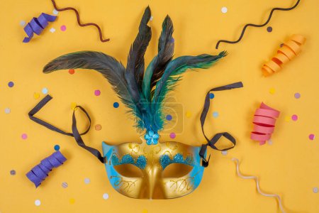Photo for White and gold mask adorned with feathers, isolated on a yellow background with colorful confetti - Royalty Free Image