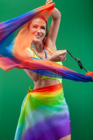Photo for Brazilian woman isolated on a green background, dancing with a colorful ribbon overflowing with joy. - Royalty Free Image