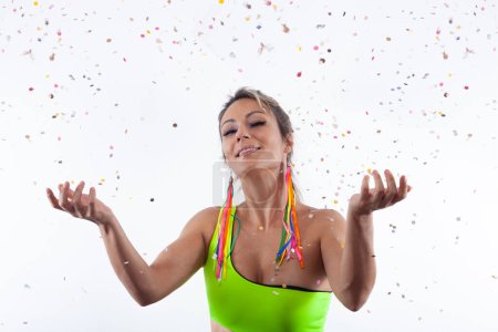 Photo for A woman with a joyful smile, adorned in vibrant clothing, stands against a white backdrop, gleefully tossing confetti into the air. - Royalty Free Image