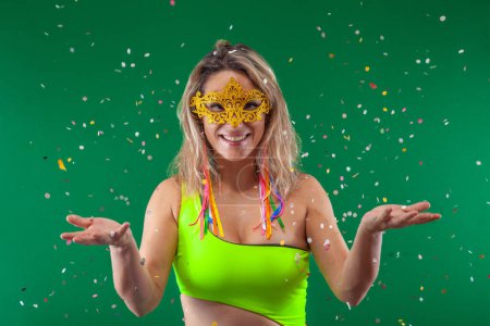 Photo for A cheerful woman, surrounded by a green backdrop, adorned in vibrant attire, joyfully releasing confetti into the air - Royalty Free Image