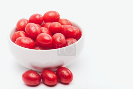 Photo for Fresh red cherry tomatoes in a white bowl and three tomatoes outside the bowl - Royalty Free Image