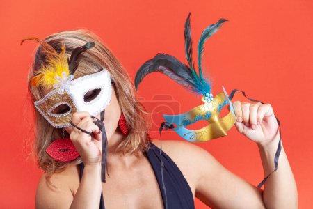 Photo for Young woman trying on colorful Venetian masks, isolated on a horizontal orange background, and wearing carnival costumes - Royalty Free Image