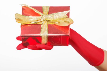 Téléchargez les photos : Main de femme avec gant rouge tenant un cadeau sur un fond blanc - en image libre de droit