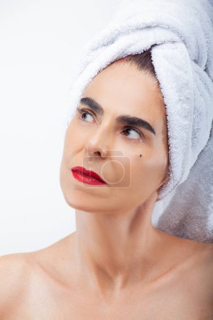 Photo for Extreme close-up of a mature woman with makeup, a white towel on her head, and a white background - Royalty Free Image