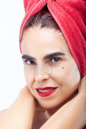 Photo for Extreme close-up of a smiling adult woman with her hands on her neck and a red towel on her head - Royalty Free Image