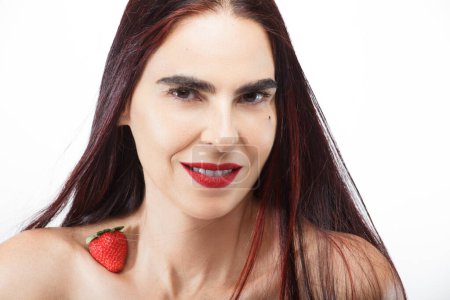 Photo for Portrait of a beautiful smiling woman with a strawberry at the end of her neck, with long hair and a white background - Royalty Free Image