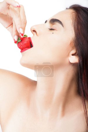 Photo for Woman in profile, with her face up, biting into a strawberry against a white background - Royalty Free Image