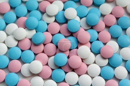 Auf dem Tisch liegen weiße, blaue und rosa Tabletten. Hintergrund