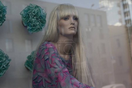 Maniquí femenino hermoso en escaparate y reflexión de la calle