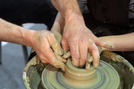 Foto de Un alfarero le enseña a un niño a trabajar con arcilla en una rueda de cerámica. Artesanía - Imagen libre de derechos