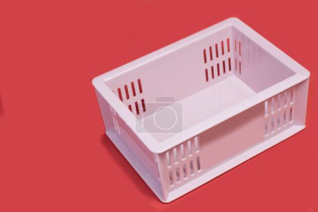 Téléchargez les photos : Une caisse en plastique contenant des objets rose clair, vide, placée sur un fond rouge, en attente d'utilisation - en image libre de droit