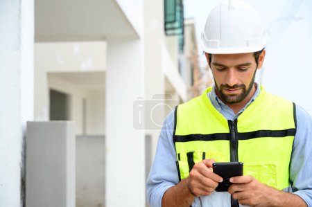 Photo for Portrait of young engineer in vest with white helmet standing on construction site, smiling and holding smartphone for worker, internet, social media - Royalty Free Image