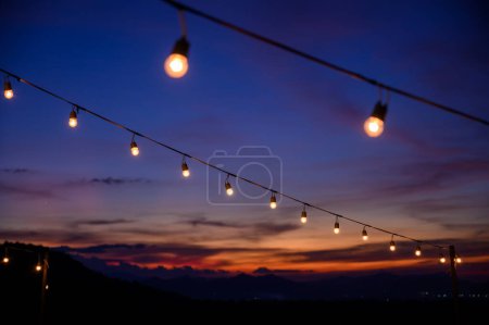 Foto de Festoon string lights decoration at the party event festival against sunset sky. light bulbs on string wire with copy space. Outdoor holiday background - Imagen libre de derechos