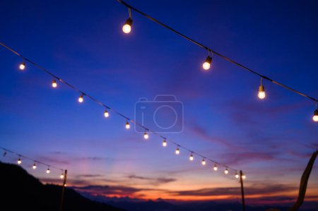 Foto de Festoon string lights decoration at the party event festival against sunset sky. light bulbs on string wire with copy space. Outdoor holiday background - Imagen libre de derechos
