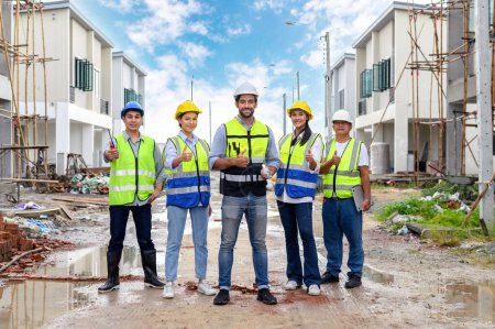 Group of happy contractors, engineers and formats in safety vests with helmets showing thumb up while standing on the under-construction building site. teamwork concept