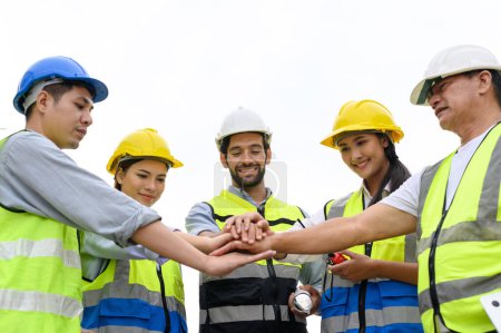 Group of contractors, engineers and formats in safety vests with helmets join hands to work together to successfully complete a construction project on construction site. cooperation and success concept