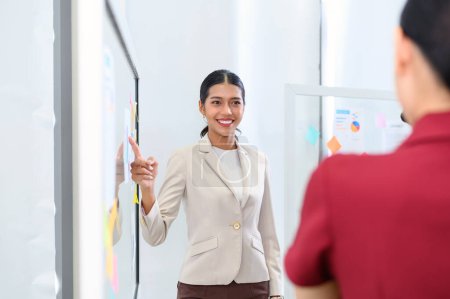 Photo for Businesswoman pointing towards graph and giving presentation explaining the idea to her business colleagues in the office. Group of Asian businesspeople brainstorm and work as team - Royalty Free Image