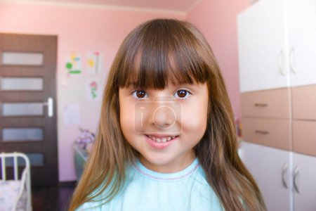 Photo for A cute girl in a blue t-shirt is smiling at the camera. Happy childhood. Child is playing in her room. - Royalty Free Image