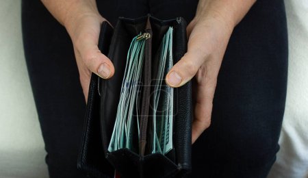 Téléchargez les photos : Un portefeuille noir avec de l'argent dans les mains d'une vieille femme. Le concept de pension élevée et de richesse élevée. - en image libre de droit