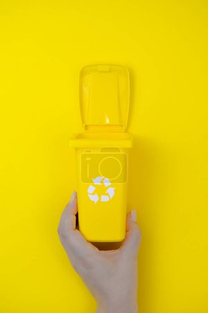 Une main tient un récipient jaune avec un couvercle recyclable, prêt pour l'élimination responsable des déchets.