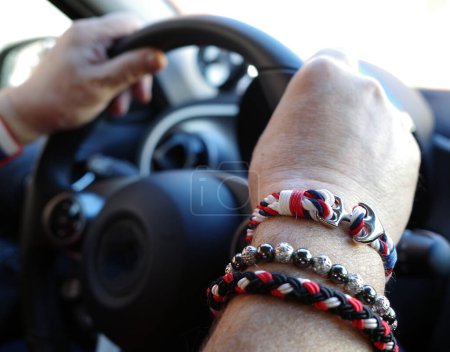 Téléchargez les photos : Les mains d'un homme avec des bracelets rouges, blancs et bleus qui dirigent une voiture - en image libre de droit