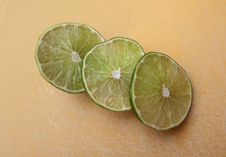 Photo for Persian lime fruit slices on an orange cutting board. Lime is a citrus fruit. This lime is a cross between key lime and lemon - Royalty Free Image