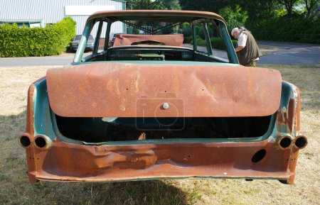 Photo for Back of a totally rusted old car with a man in the background photographing it - Royalty Free Image