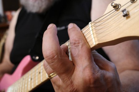 Photo for The hand of a man who plays  a chord on a pink guitar with steel strings - Royalty Free Image