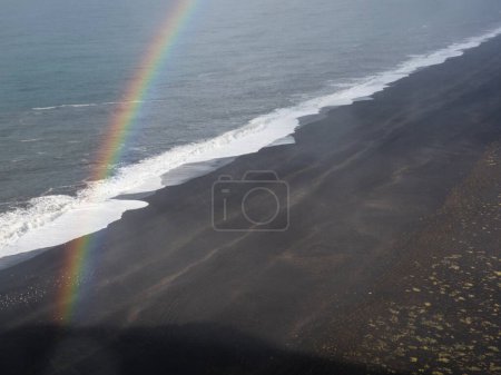 Regenbogen am schwarzen Sandstrand Solheimafjara in Vik, Island